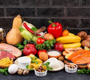 Balanced whole foods against a dark brick wall: salmon, chicken, eggs, vegetables, fruit, grains and dairy